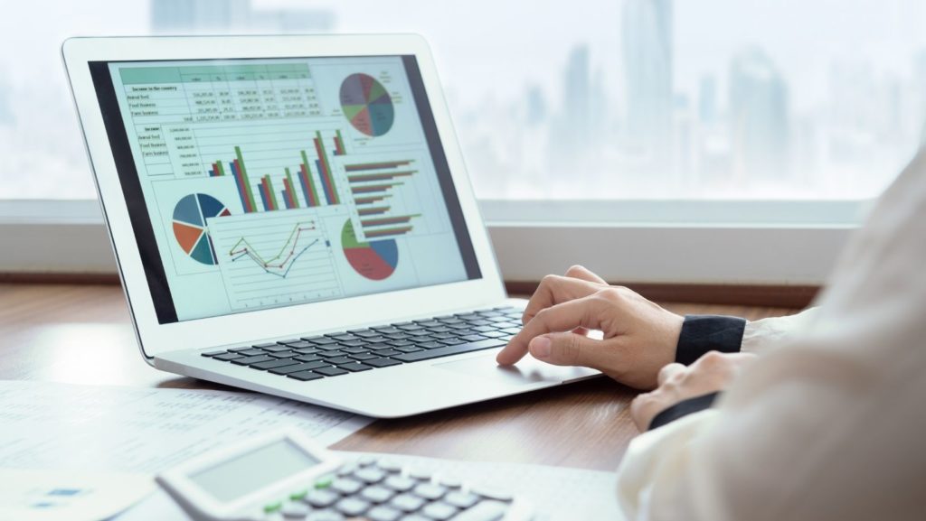 Laptop open with a range of graphs and reports and a woman's hand on the track pad