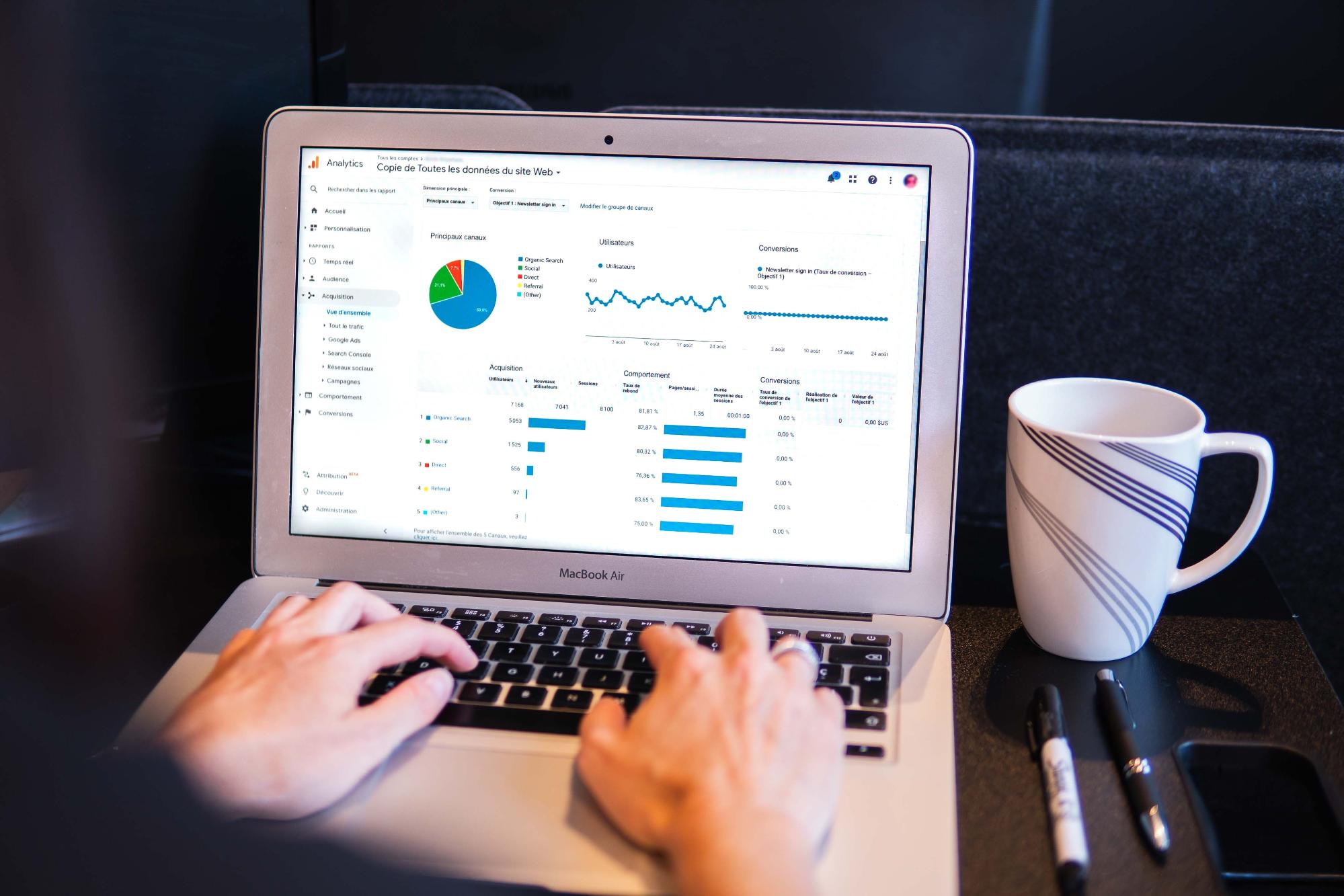 Laptop with hands and there are bar graphs and a pie chart on the screen