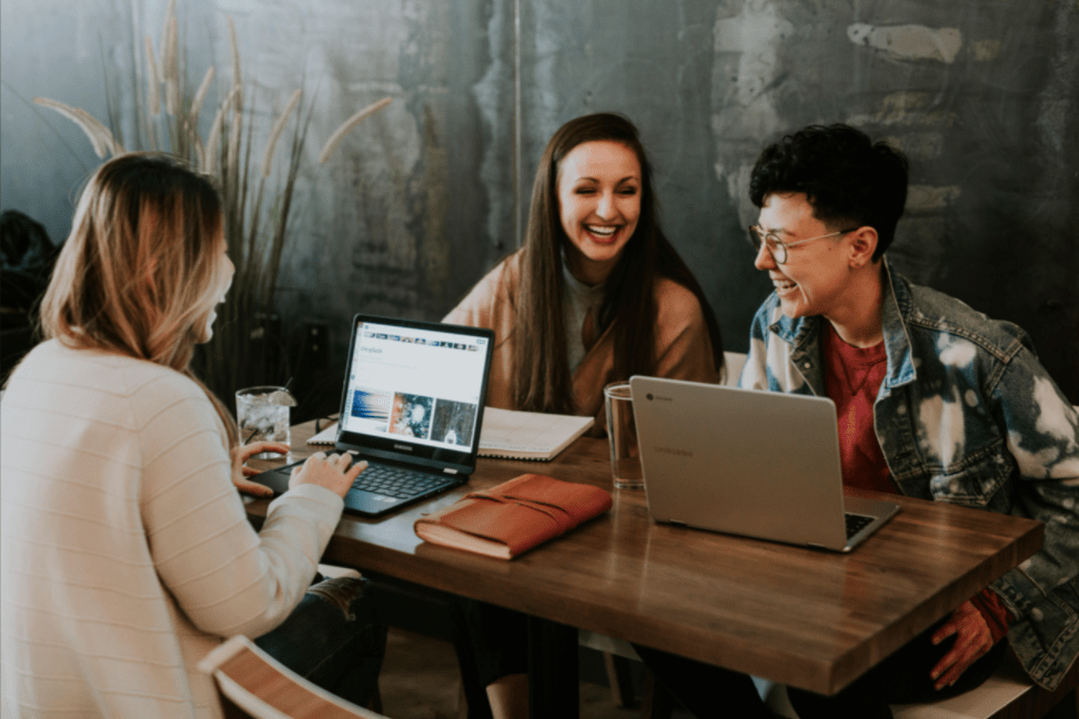 Three international women sitting around a table with laptops working on SEO strategies.